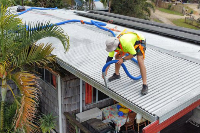 Photo of man in high vis gear, working on roof with extended vacuum hose