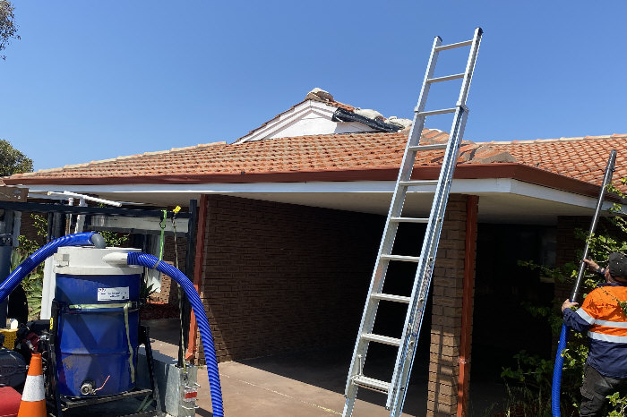 Front elevation of house whilst worker cleaning gutters and storage tank