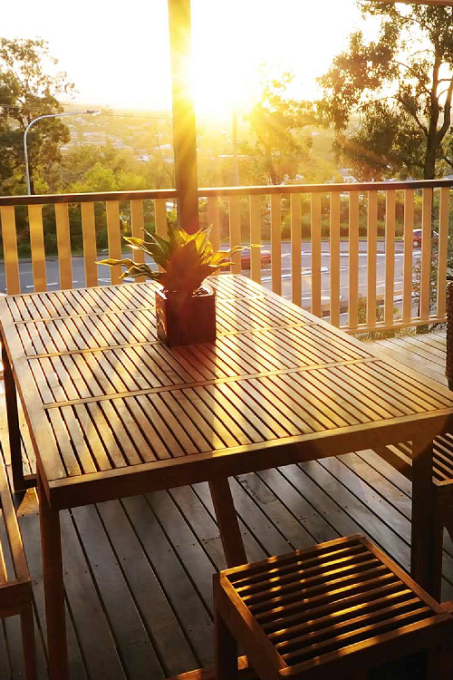 Photo of beautiful verandah, with outdoor lounges and wooden table overlooking bush land during sunset